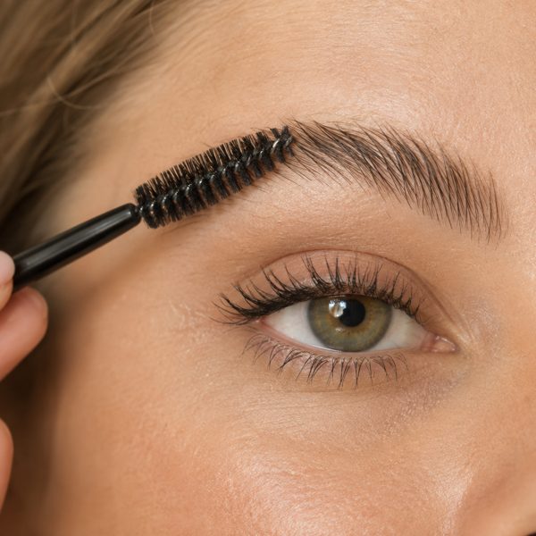 Close-up of a brow being brushed up and out with a spoolie, illustrating the brow-lift step (AI-generated image)